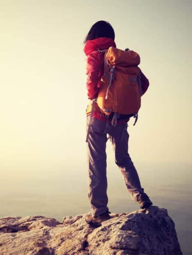 Female hiker with backpack standing on seaside cliff Stock
