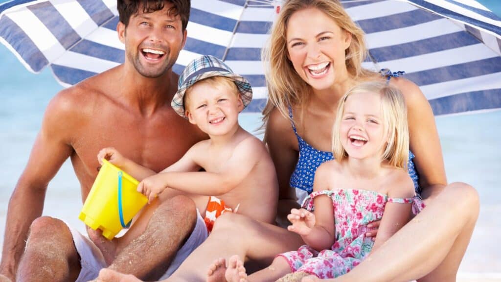 Family Sheltering From Sun Under Beach Umbrella Stock