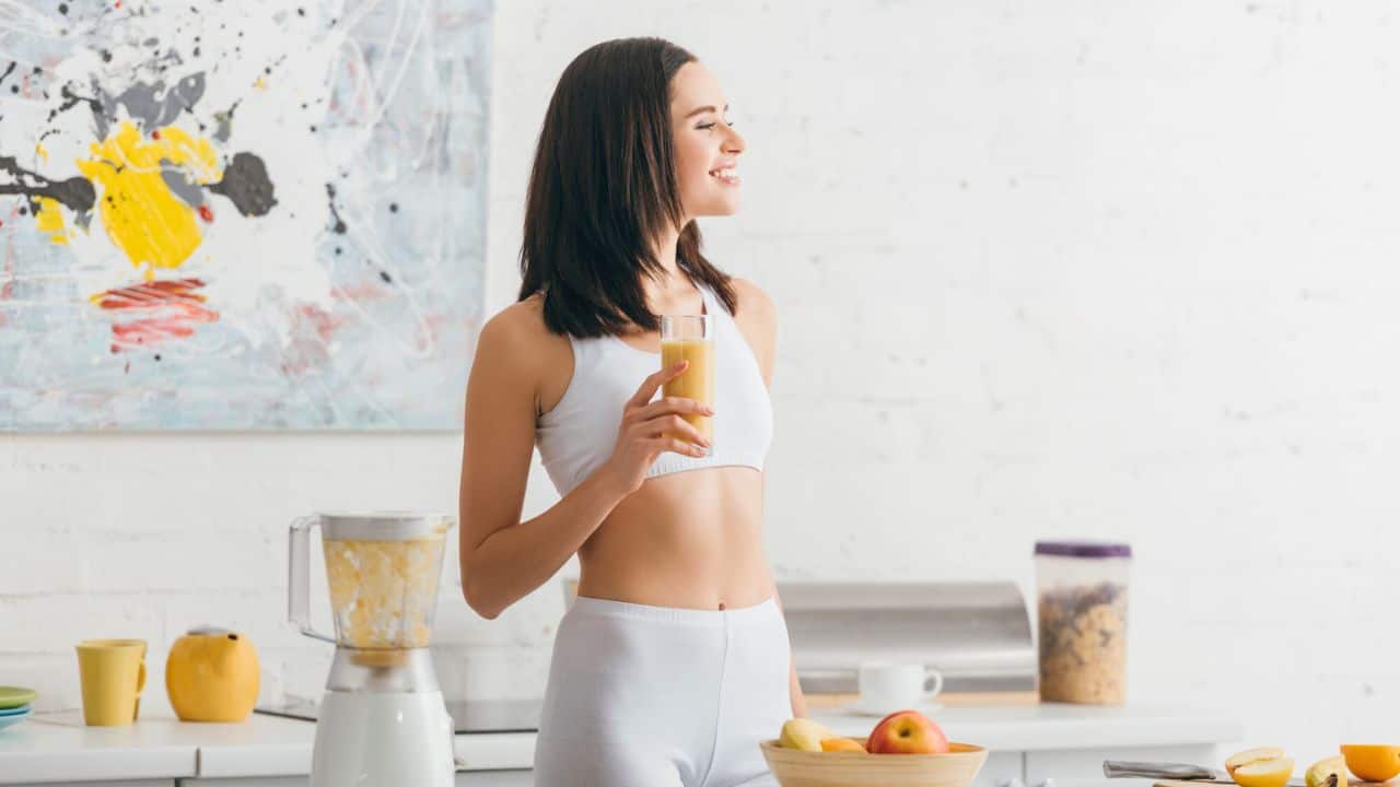 Attractive fit sportswoman smiling and holding glass of smoothie stock