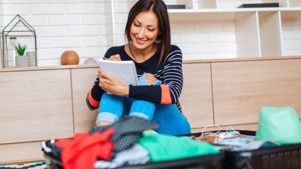 Beautiful young woman packing her stuff into a big luggage stock
