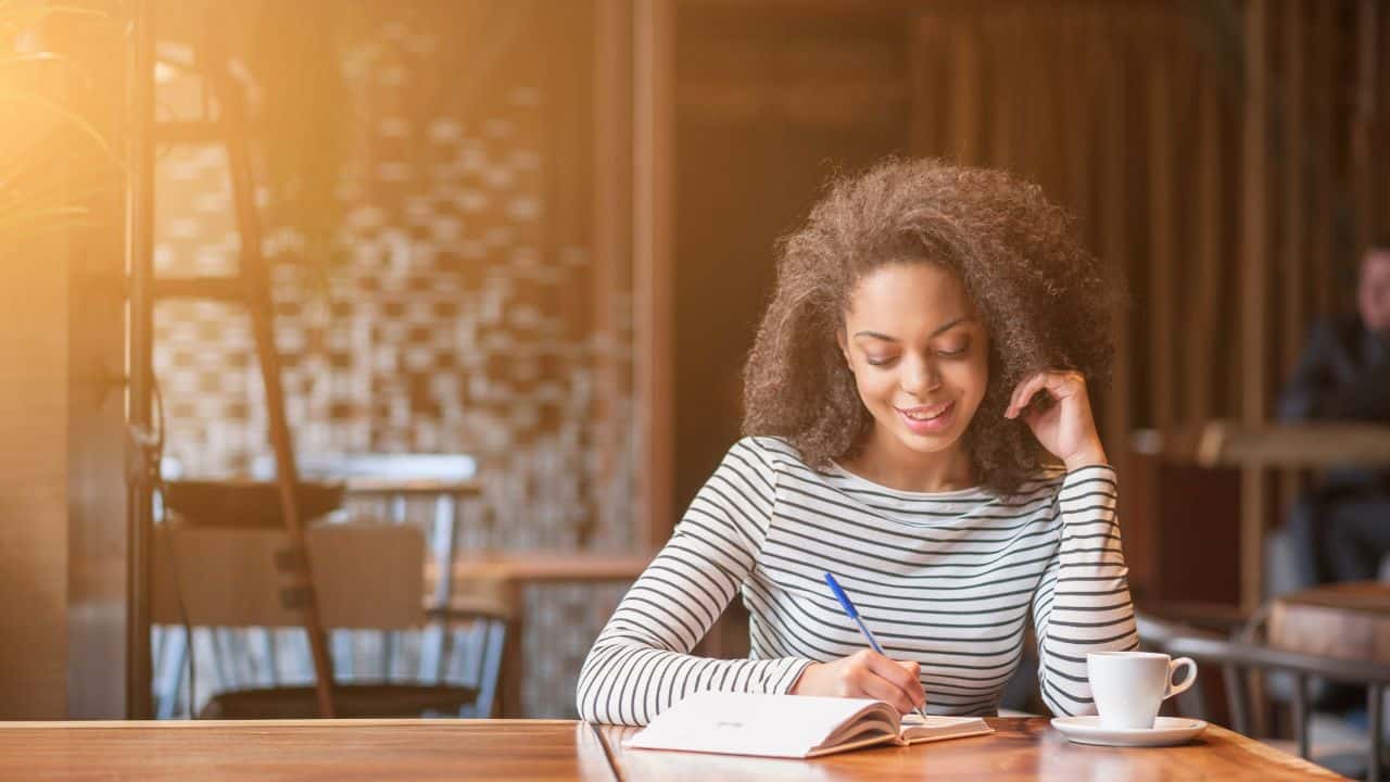 Cheerful young woman is writing in notebook stock