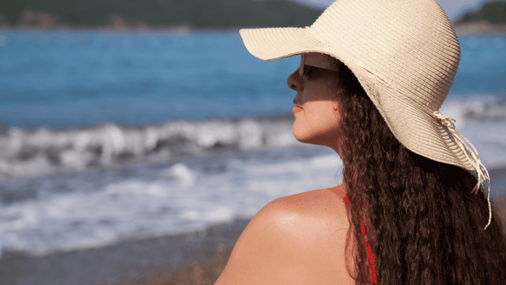 A Beautiful Woman in a Hat Sits on a Pebble Beach Stock